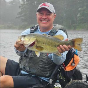 Smiling kayak angler Jason A. holding a large largemouth bass fishing from a Hobie Kayak with a foggy lake in the background.