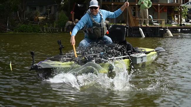 DustyNettingFish Dusty Yakker nets a fish while kayak fishing in a scenic lake.